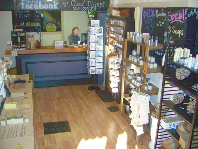 All Good Things homemade all natural soap products, picture of owner operator at front desk, at 318 West Main Street, Madison Historic District Indiana 47250. Picture includes view of display inventory along a wall and post card stand.