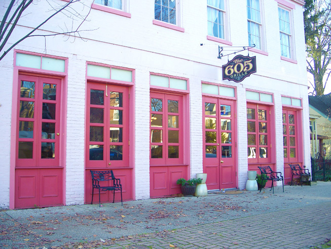 The 605 Grille, dinner only restuarant and pub’s front exterior of building with rose red doors and benches.